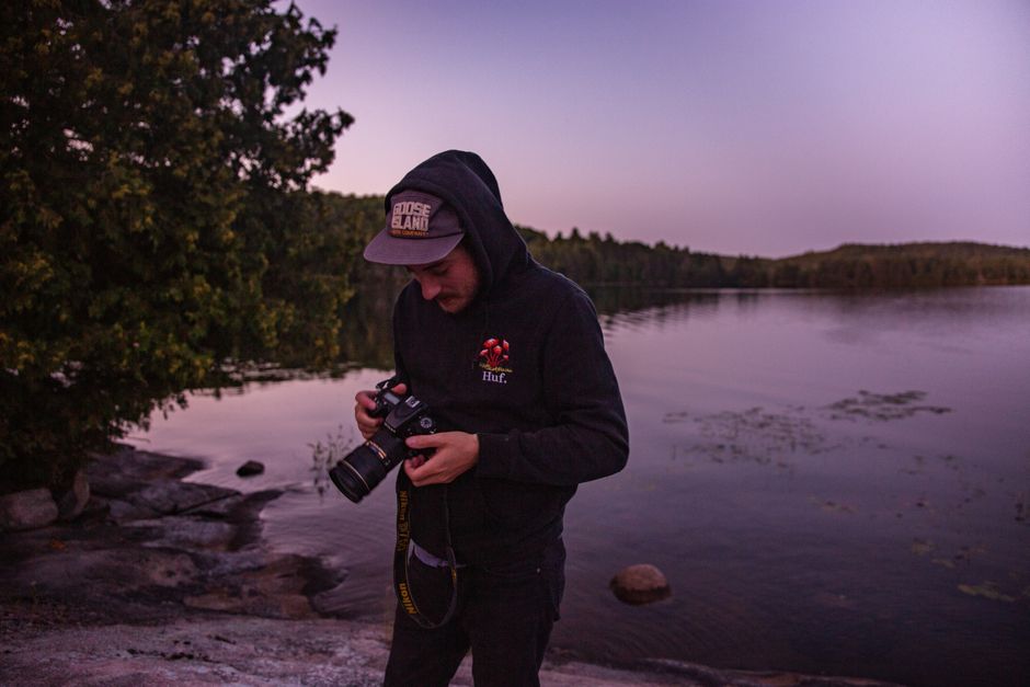 A man with a camera stands by a tranquil lake during twilight, capturing nature's serenity.